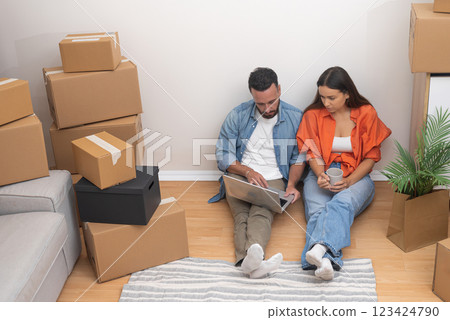 Happy newlyweds celebrate purchase of new flat together sitting on floor with carpet among things collected in carton boxes after receiving keys from agent Happy newlyweds celebrate purchase of new flat together sitting on floor with carpet among things collected in carton boxes after receiving keys from agent 123424790