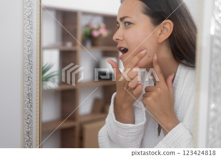 A distressed woman gazes into the bathroom mirror, feeling unhappy about her skin concerns.  123424818