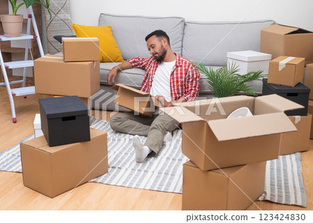 In the midst of moving, a young man unboxes his possessions, encapsulating the essence of relocation, whether for rentals or home ownership 123424830