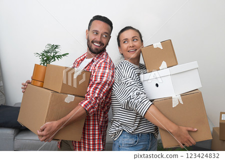 Moving as Tenants: A young couple, renting their new place, carries a stack of cardboard relocation boxes into the living room, determined to settle in 123424832