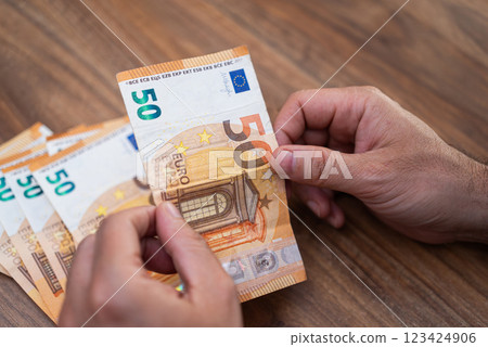 Male entrepreneur hands hold euro banknote counting money benefiting from currency exchange service with favorable rate sitting at wooden desk in company office Male entrepreneur hands hold euro banknote counting money benefiting from currency exchange service with favorable rate sitting at wooden desk in company office 123424906