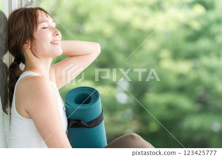 A woman taking deep breaths and forest bathing with a yoga mat in a forest or park (yoga, pilates, health care, refreshment) 123425777