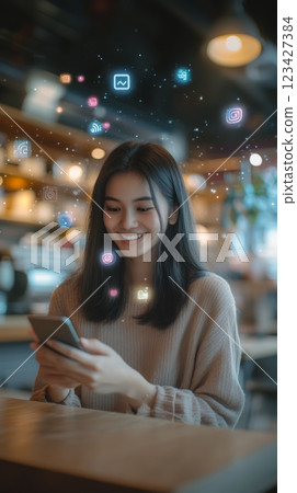 Young woman is smiling while using her smartphone at a cafe, surrounded by glowing social media icons, representing her engagement with online platforms and digital communication 123427384