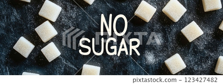 White sugar cubes scattered around the text no sugar written on a dark background promoting a sugar free or low sugar lifestyle for better health and wellness 123427482