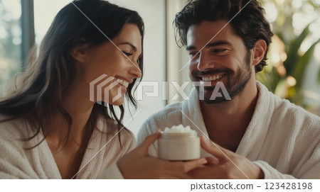 Smiling couple wearing bathrobes shares a moment of self care, holding a jar of moisturizer, enjoying their skincare routine together in a bright, comfortable setting Smiling couple wearing bathrobes shares a moment of self care, holding a jar of moisturizer, enjoying their skincare routine together in a bright, comfortable setting 123428198