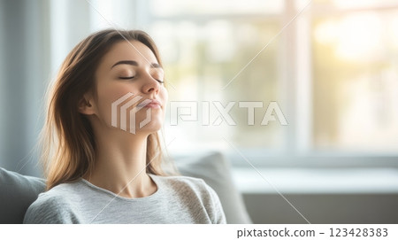Woman meditating and breathing deeply, relaxing on sofa at home, feeling peaceful and stress free 123428383