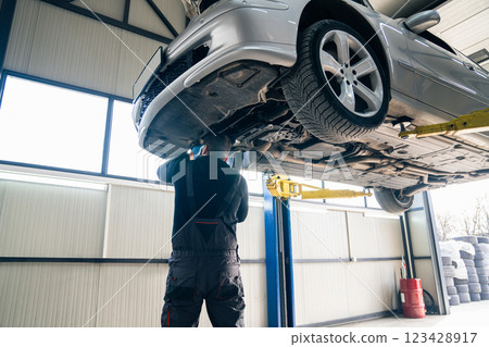 Serviceman checks car suspension on a column lift in car service 123428917