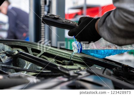 Serviceman adds windshield washer fluid in car service 123428973
