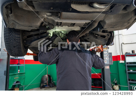 Serviceman checks car suspension on a column lift in car service Serviceman checks car suspension on a column lift in car service 123428993