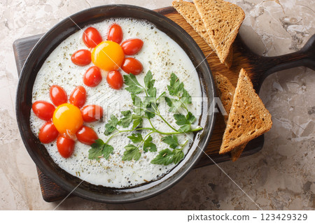 Flower shaped breakfast idea cooked fried eggs, parsley and cherry tomatoes close-up in a plate. Horizontal top view 123429329