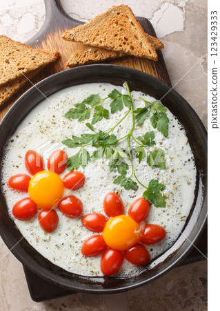 Children's breakfast of fried eggs, cherry tomatoes and parsley in the shape of a flower close-up in a plate. Vertical top view 123429333