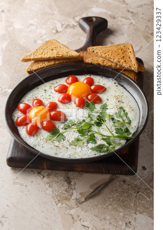 Children's breakfast of fried eggs, cherry tomatoes and parsley in the shape of a flower close-up in a plate. Vertical Children's breakfast of fried eggs, cherry tomatoes and parsley in the shape of a flower close-up in a plate. Vertical 123429337