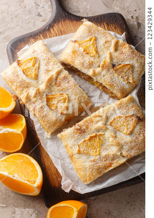 Orange strudel pie with jam, nuts, raisins and fresh fruits close-up on wooden board on table. Vertical top view 123429344