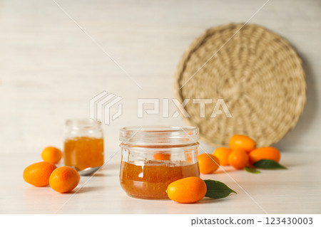 Kumquat and jar of jam on light wooden background 123430003