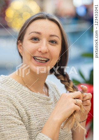 Caucasian woman with braces on her teeth braids her hair.  123431041