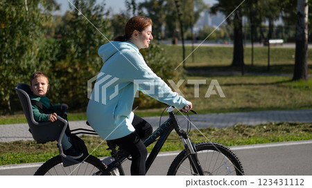 Caucasian woman riding a bicycle with her toddler son sitting behind her in a child seat. Caucasian woman riding a bicycle with her toddler son sitting behind her in a child seat. 123431112