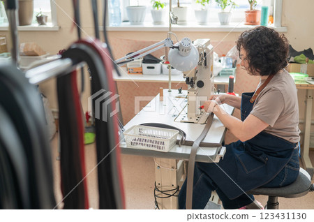 A woman tanner sews a leather belt on a sewing machine.  123431130