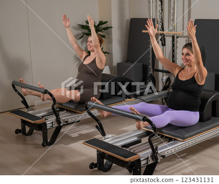 Two pregnant women do Pilates exercises on a reformer. Yoga class for pregnant women.  123431131