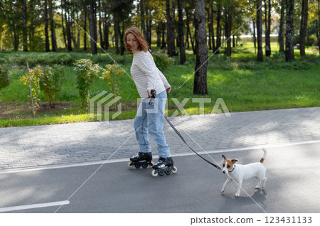 Caucasian woman roller skating with her jack russell terrier dog in park.  123431133