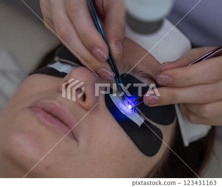 A woman undergoing eyelash extension procedure using an ultraviolet lamp. 123431163