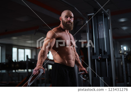 Bald Caucasian bodybuilder training chest using cable crossover in gym.  123431276