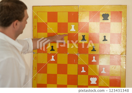 Caucasian man standing at wall mounted magnetic chessboard demonstration. Caucasian man standing at wall mounted magnetic chessboard demonstration. 123431348