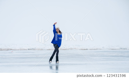Caucasian woman in a blue sweater is skating on a frozen lake. The figure skater performs the program. 123431596