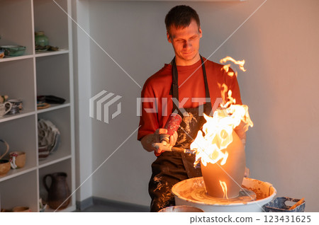 A potter burns a jug with a gas burner on a potter's wheel. A potter burns a jug with a gas burner on a potter's wheel. 123431625