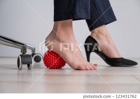 Business woman massages her feet on a massage ball with spikes. 123431762