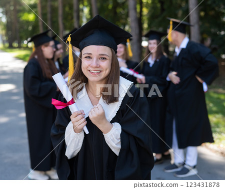 Group of happy students in graduation gowns outdoors. A young girl is happy to receive her diploma. Group of happy students in graduation gowns outdoors. A young girl is happy to receive her diploma. 123431878