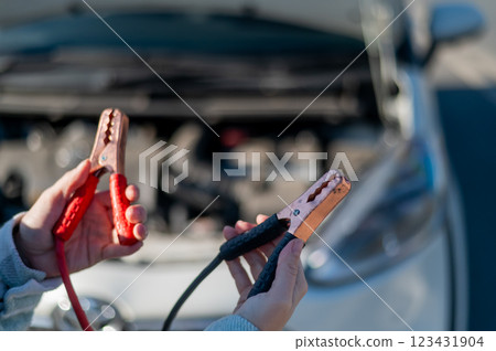 Woman holding clamps for charging a car battery.  123431904