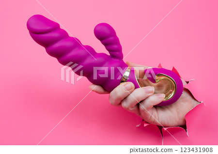 Female hand sticking out with pink sex toy from pink paper background. Female hand sticking out with pink sex toy from pink paper background. 123431908