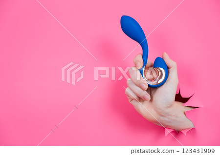 Hand with blue vibrator sticking out through pink paper background.  123431909