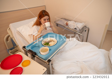 Caucasian woman eats on hospital bed after giving birth. Caucasian woman eats on hospital bed after giving birth. 123432011