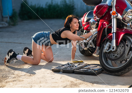 Brunette woman in denim shorts repairs a red motorcycle.  123432070