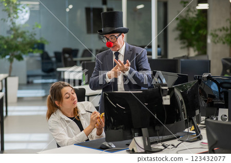 Caucasian woman works at the computer. Elderly man in clown costume in office. Caucasian woman works at the computer. Elderly man in clown costume in office. 123432077