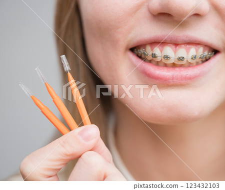 Close-up portrait of a woman with braces holding a floss to clean her teeth. Close-up portrait of a woman with braces holding a floss to clean her teeth. 123432103