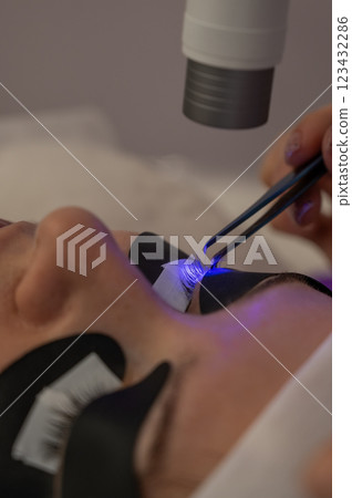 A woman undergoing eyelash extension procedure using an ultraviolet lamp. A woman undergoing eyelash extension procedure using an ultraviolet lamp. 123432286