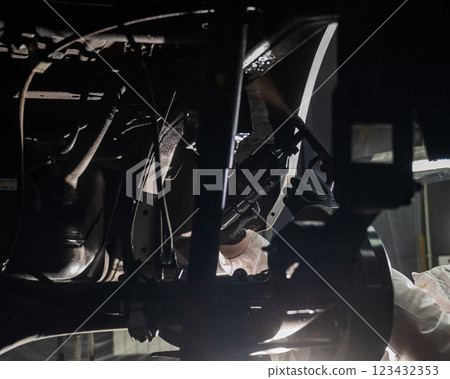 An auto mechanic applies anti-corrosion mastic to the underbody of a car. 123432353