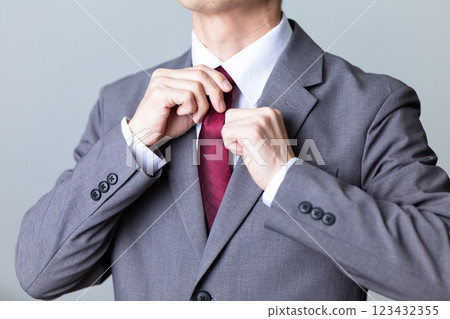 A middle-aged male businessman wearing a gray suit and fixing his tie 123432355