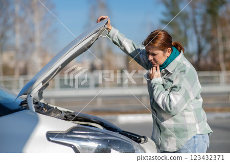 Caucasian woman looks puzzled under the hood of a car.  123432371