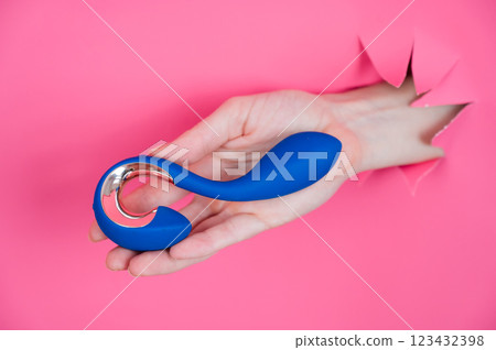 Hand with blue vibrator sticking out through pink paper background.  123432398