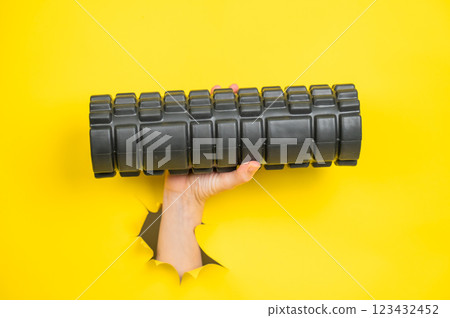 Female hand sticking out with MFR roller from yellow paper background. 123432452