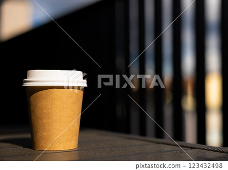 A paper coffee cup with white lid stands on black table outside Sunny summer day 123432498