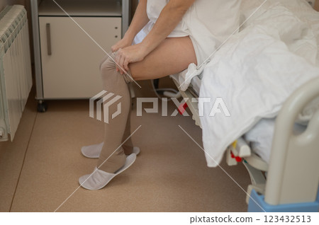 A woman puts on post-operative compression stockings in a hospital room.  123432513