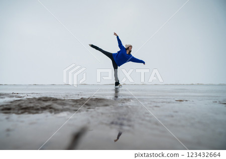 Caucasian woman in a blue sweater is skating on a frozen lake. Figure skater performs a swallow. Caucasian woman in a blue sweater is skating on a frozen lake. Figure skater performs a swallow. 123432664