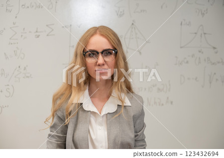 A Caucasian woman stands at a blackboard with written formulas. 123432694