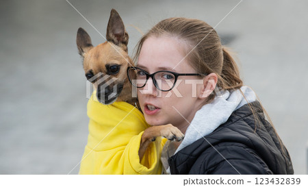 Portrait of a young Caucasian woman hugging a small dog in a jacket.  123432839