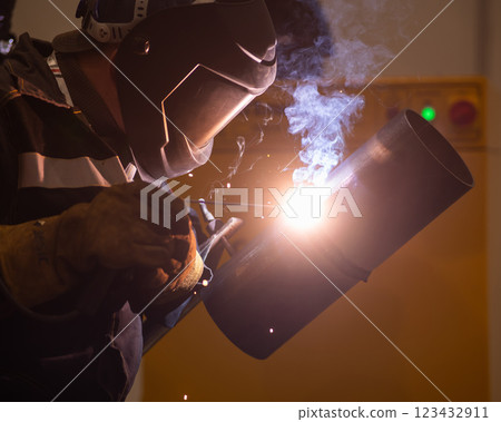 A man wearing a protective mask welds a metal pipe.  123432911