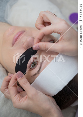 The master applies protective patches that do not let in ultraviolet rays before LED eyelash extensions. Vertical photo.  123433035